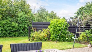 Ein Holztisch mit einem Strauß violetter Blumen, eine schwarze Metallschaukel und ein Holzzaun in einem Garten.