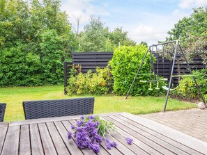 A wooden table with a bouquet of purple flowers, a black metal swing set, and a wooden fence in a garden. - 6 Person Holiday Home in Skjern (Skjern)
