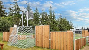 Een sportveld met een basketbalring, omgeven door een houten omheining en een metalen poort.