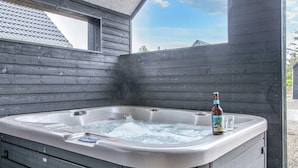 Een hottub met een fles en glazen, houten wanden en uitzicht op een heldere lucht.