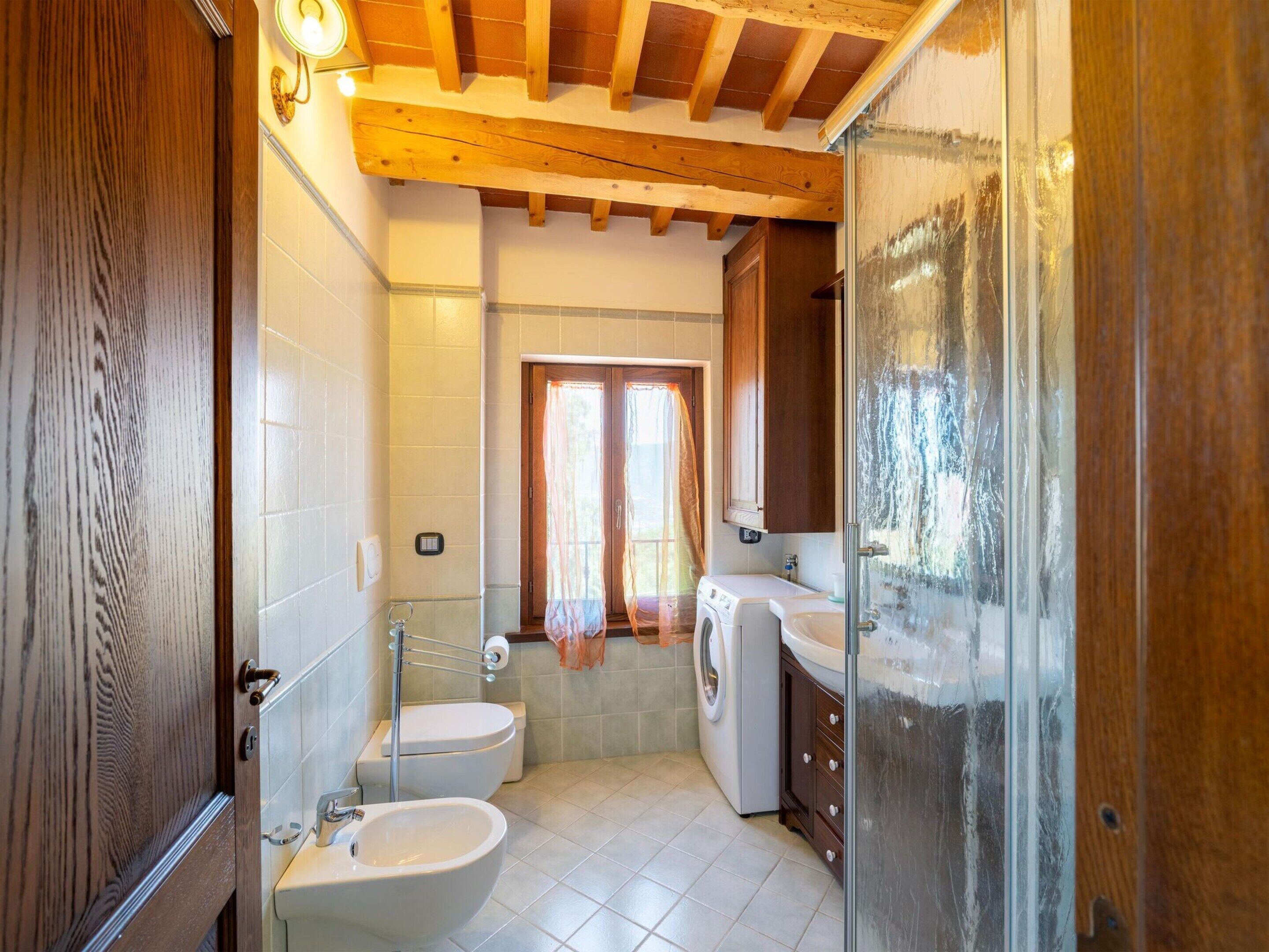 A bathroom with a wooden ceiling, a toilet, a bidet, a washing machine, and a sink.