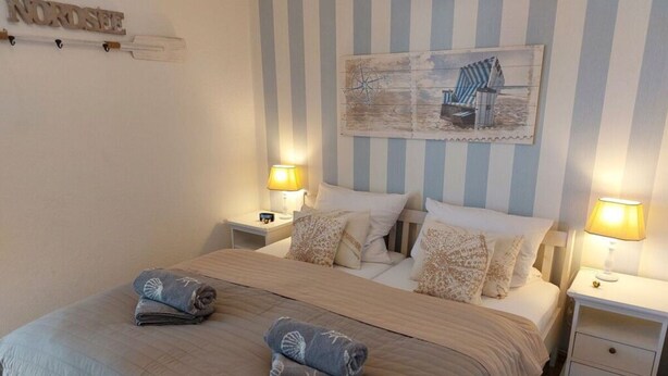 A neatly made bed with two pillows and two folded towels, a striped wall, and a small painting above the bed. - Sky Blue Comfortable Holiday Residence (Friedrichskoog)