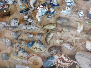 Eine Auswahl an Tierfiguren und Muscheln, darunter Seeotter und Seesterne, auf einer sandigen Fläche angeordnet.