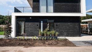 Una casa moderna de dos pisos con techo plano, ventanas grandes y un balcón.