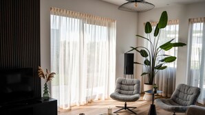 Una sala moderna con televisor de pantalla plana, dos sillones grises, una mesita de centro y una planta grande.