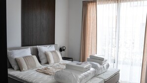 Un dormitorio moderno con una cama grande, una mesita de noche, una lámpara de pared y cortinas traslúcidas.