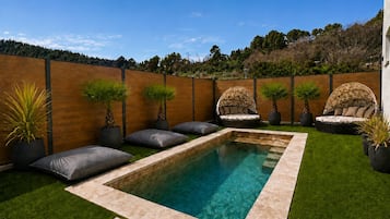 Ein rechteckiger Swimmingpool mit Holzterrasse, umgeben von Rasen und Kübelpflanzen.
