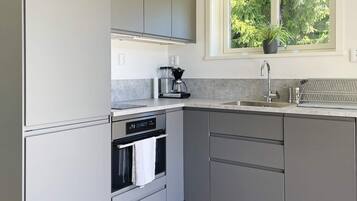 Cozinha moderna com armários cinza, forno embutido, cafeteira e janela com vista para o verde.