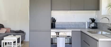 Una cocina compacta con gabinetes grises, horno integrado y cafetera.