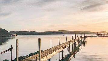 A wooden pier extending into calm water with a hilly landscape in the background.