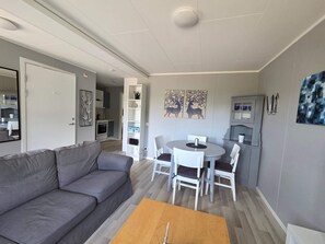Uma sala de estar moderna com um sofá cinzento, uma mesa de centro de madeira e um espaço de jantar com cadeiras brancas e uma mesa redonda.