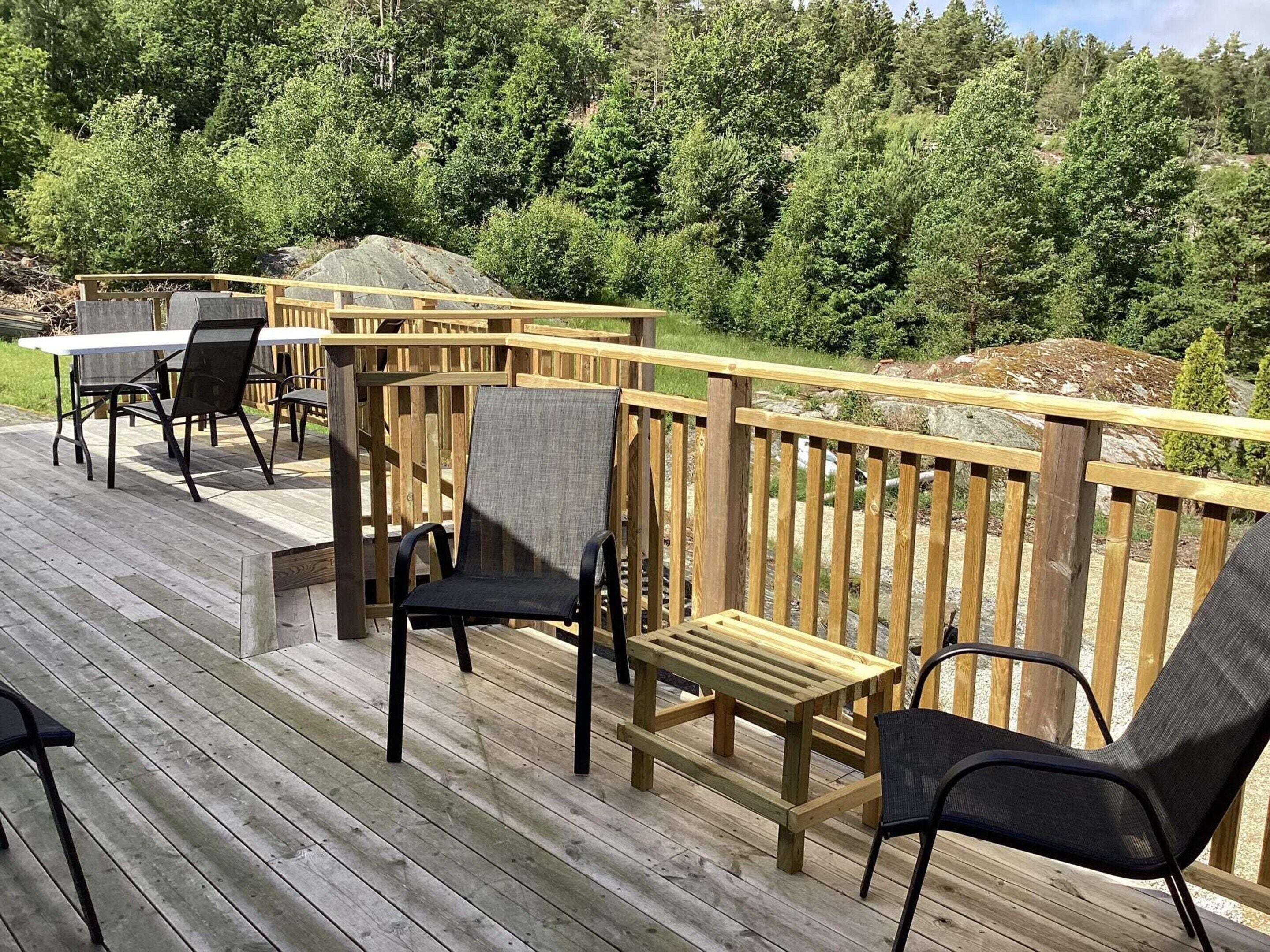 A wooden deck with outdoor furniture, including chairs and a table, overlooking a forested area.