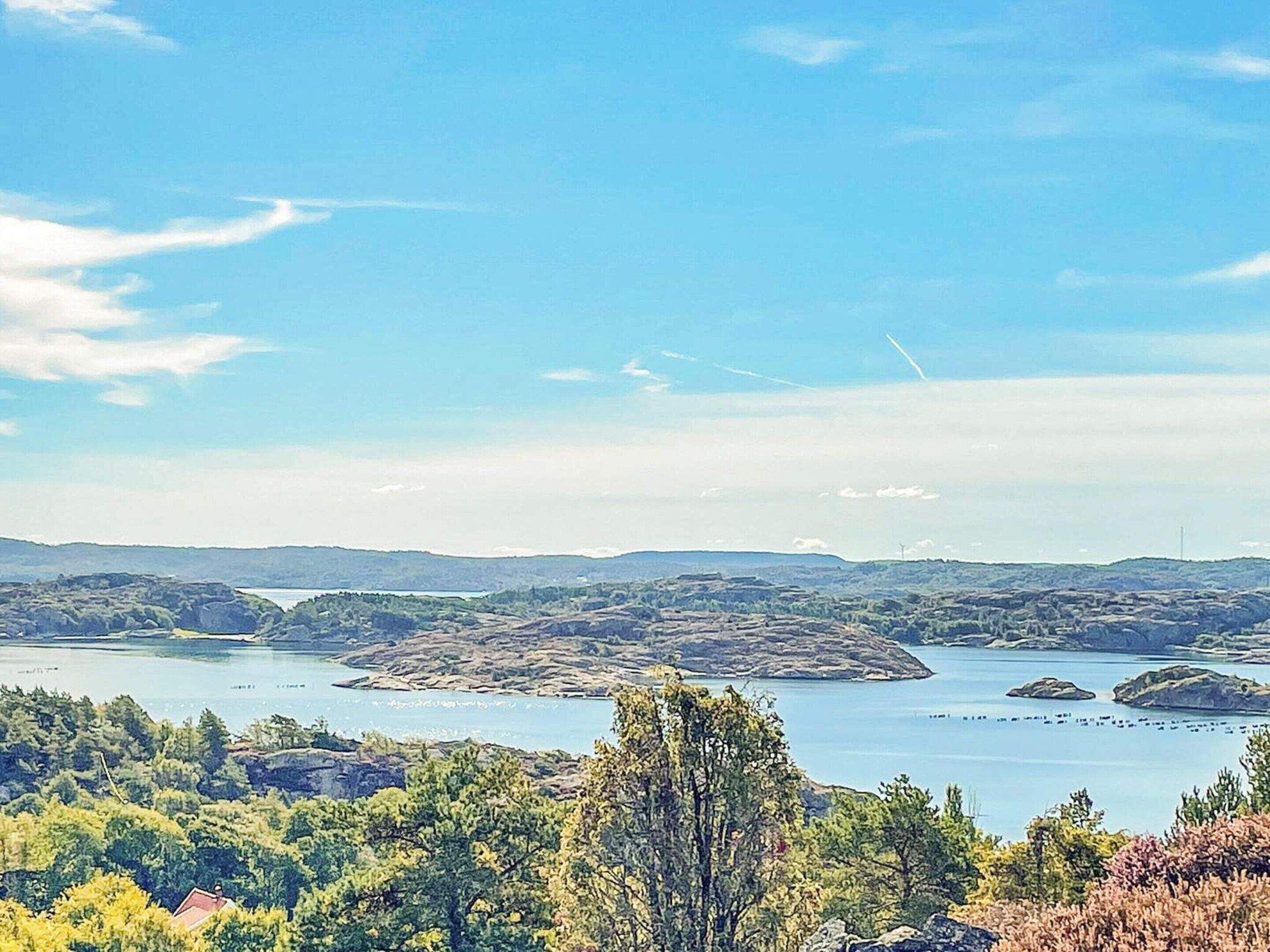 Et panorama over et kystlandskab med klar himmel, en sø og bakker i baggrunden.