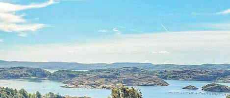 Et panorama over et kystlandskab med klar himmel, en sø og bakker i baggrunden.