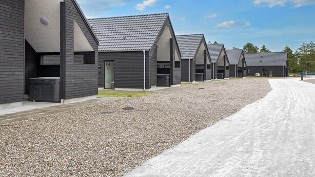 A row of modern, dark-colored buildings with pitched roofs, arranged in a linear fashion along a gravel path. - 5 Star Holiday Home in Romo (Rømø)