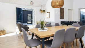A modern dining area with a wooden table and grey chairs, a hanging light fixture, and a foosball table. - 5 Star Holiday Home in Romo (Rømø)