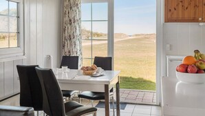 A dining area with a table, chairs, and a view of a grassy landscape through large windows. - 4 Star Holiday Home in Fjerritslev (Fjerritslev)
