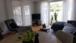 Un salon avec un canapé, des fauteuils, un téléviseur et une table sur laquelle est posée une plante.