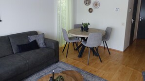 Un salon moderne avec un canapé gris, une table de salle à manger ronde en bois et quatre chaises, ainsi qu’une table basse agrémentée d’un vase et d’une bougie.