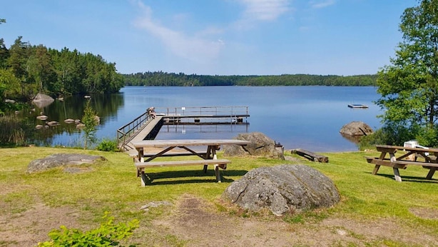 A lakeside picnic area with wooden benches and picnic tables, surrounded by rocks and greenery. - 4 Star Holiday Home in Karlskrona (Karlskrona)