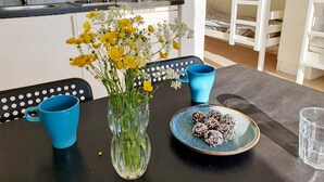 A dining area with a table set for two, featuring a vase with yellow flowers, two blue cups, and a plate of chocolate-covered treats. - 4 Star Holiday Home in Karlskrona (Karlskrona)
