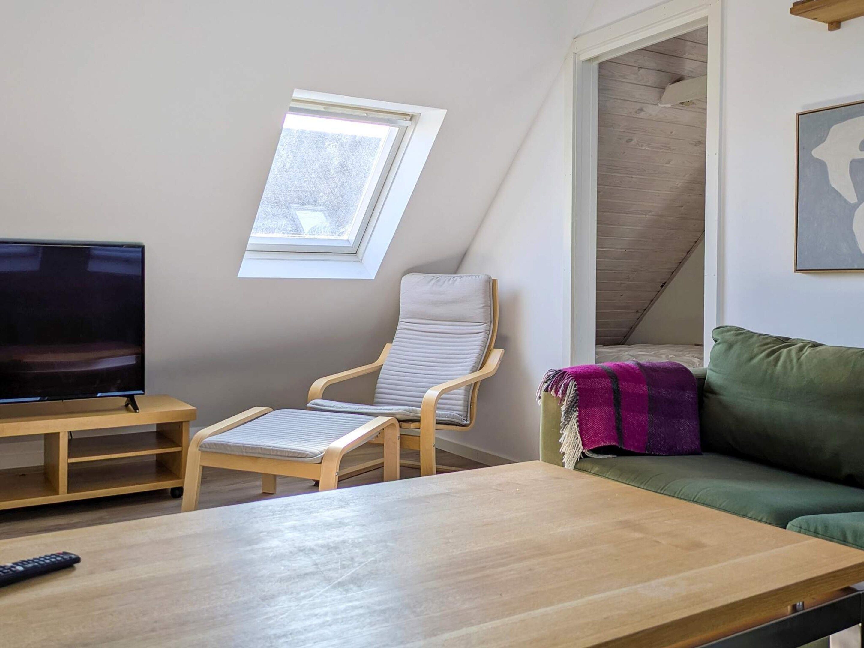 Huoneessa on televisio, puinen pöytä, pehmustettu tuoli, sohva ja ikkuna.
