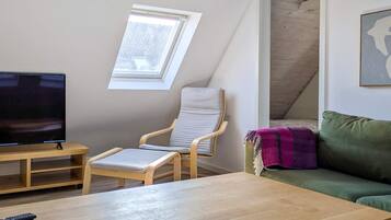 A room with a TV, a wooden table, a cushioned chair, a sofa, and a window.