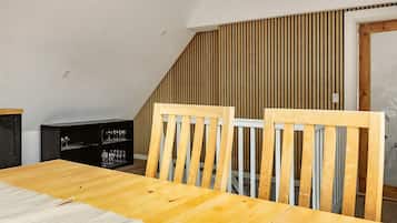 Et spiseområde med et træbord og stole, et sort skab med glas, og et skråt loft med træpaneler.