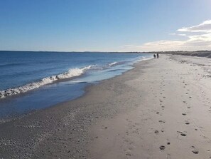 En strand med klart skint, sand og fodspor, der fører ud i vandet.