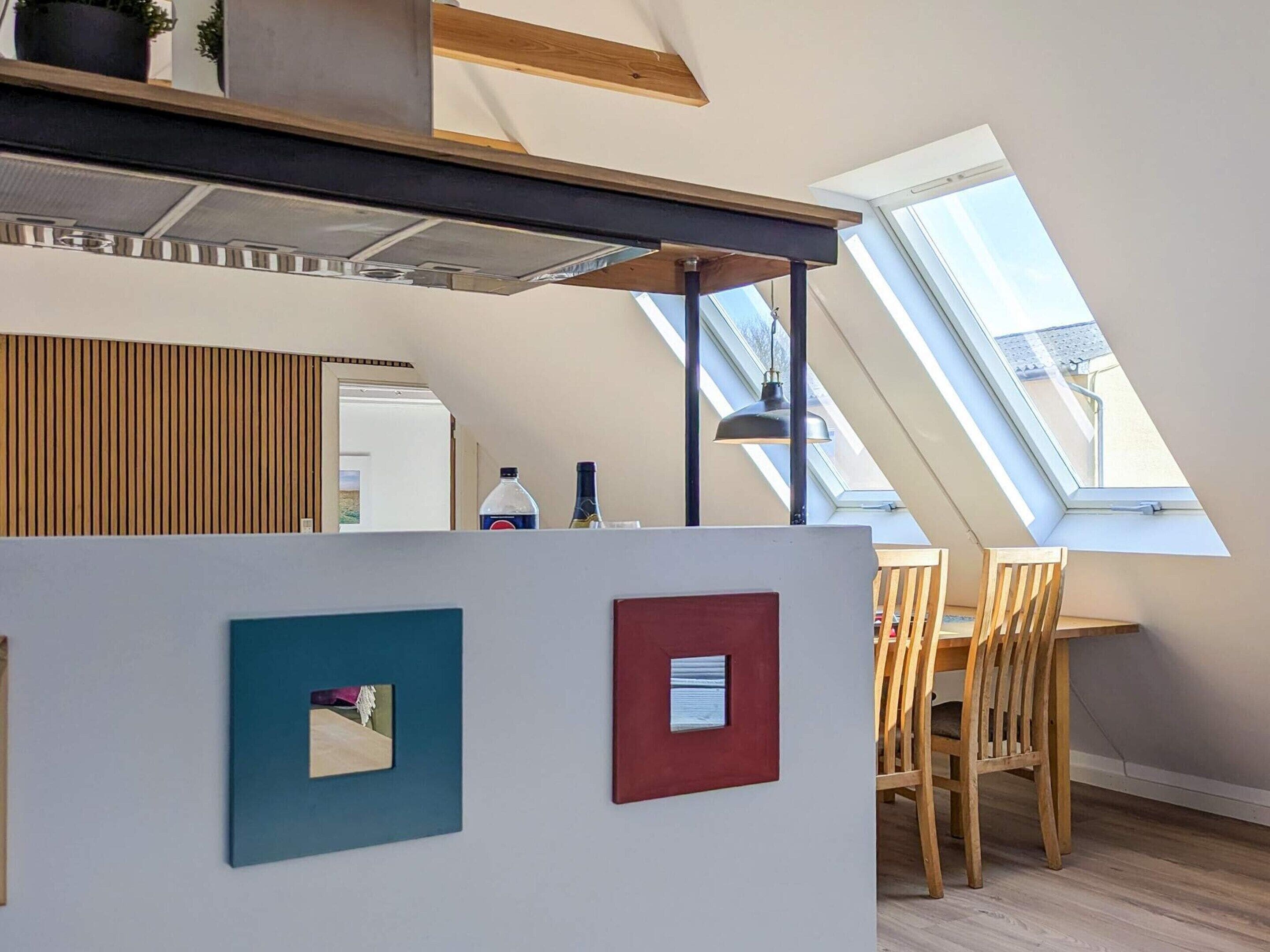 A modern kitchen with a skylight, wooden ceiling beams, and a dining area with a table and chairs.