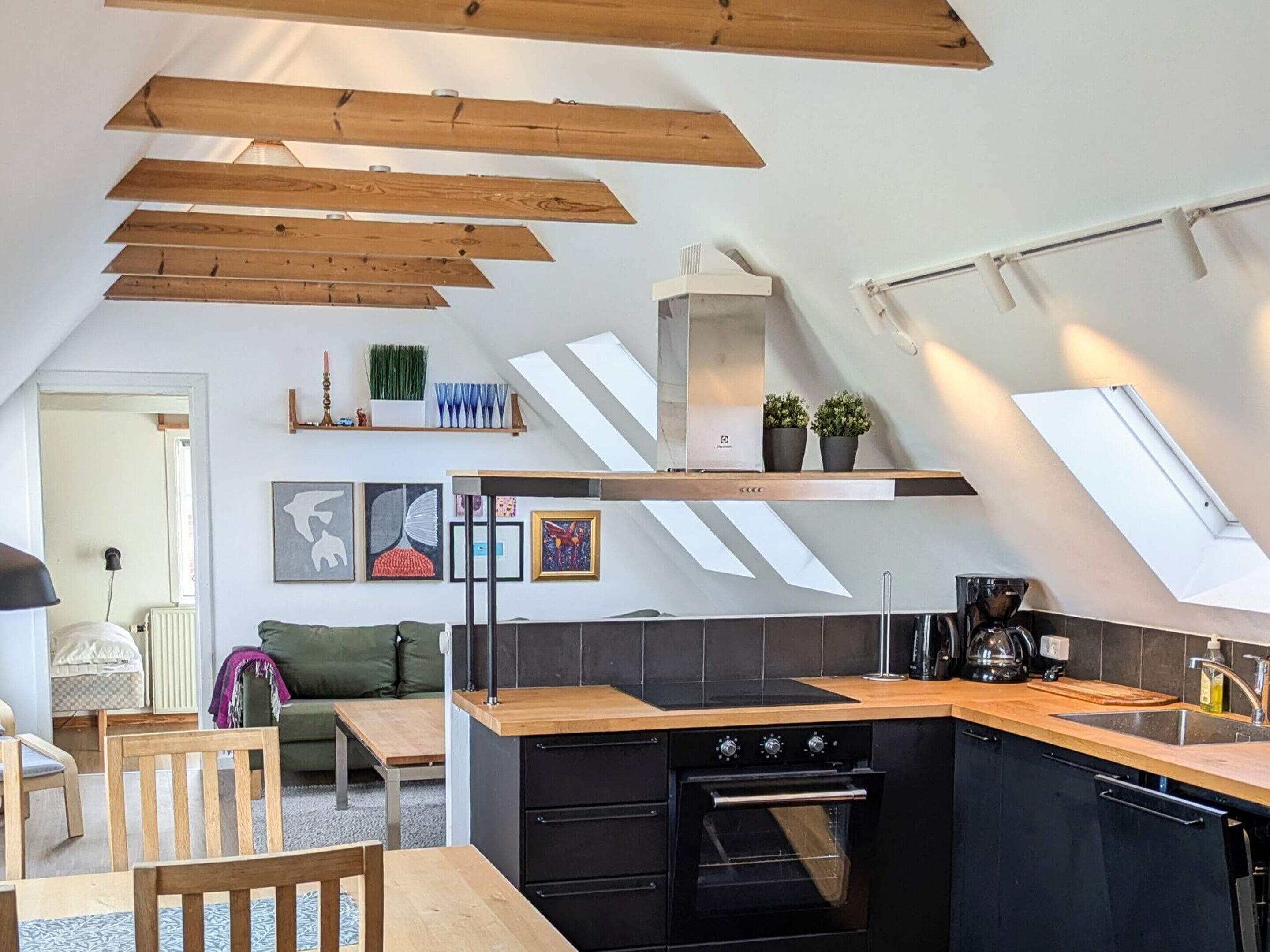 A modern kitchen with a sloped ceiling, built-in oven, and wooden beams.