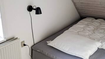 A small, single-bed room with a sloped ceiling, a white radiator, and a black wall-mounted lamp.