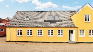A yellow building with a tiled roof, multiple windows, and a door.