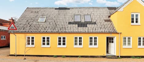 Un bâtiment jaune avec un toit recouvert de tuiles, de nombreuses fenêtres et une porte.