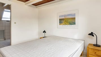 Ein Schlafzimmer mit einem Bett, zwei Nachttischen, einem hölzernen Kopfteil, einer Decke mit Holzbalken, einem gerahmten Bild an der Wand und einem Heizkörper.