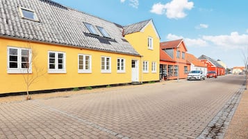 A street with yellow and red buildings, a paved road, and parked cars.