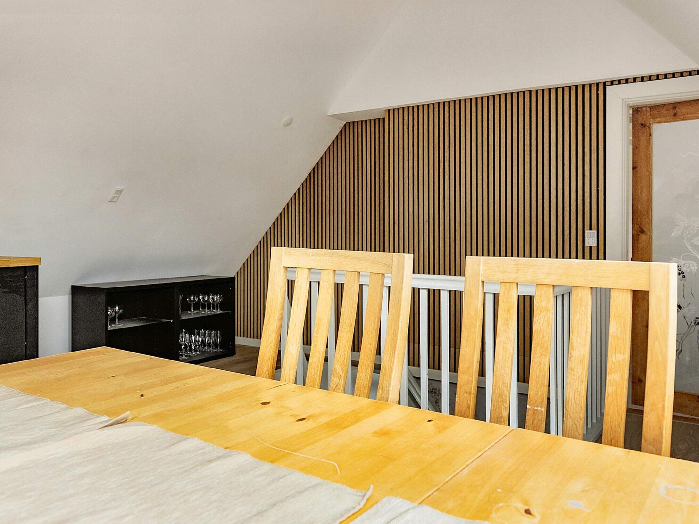 A dining area with a wooden table and chairs, a black cabinet with glassware, and a sloped ceiling with wooden paneling.