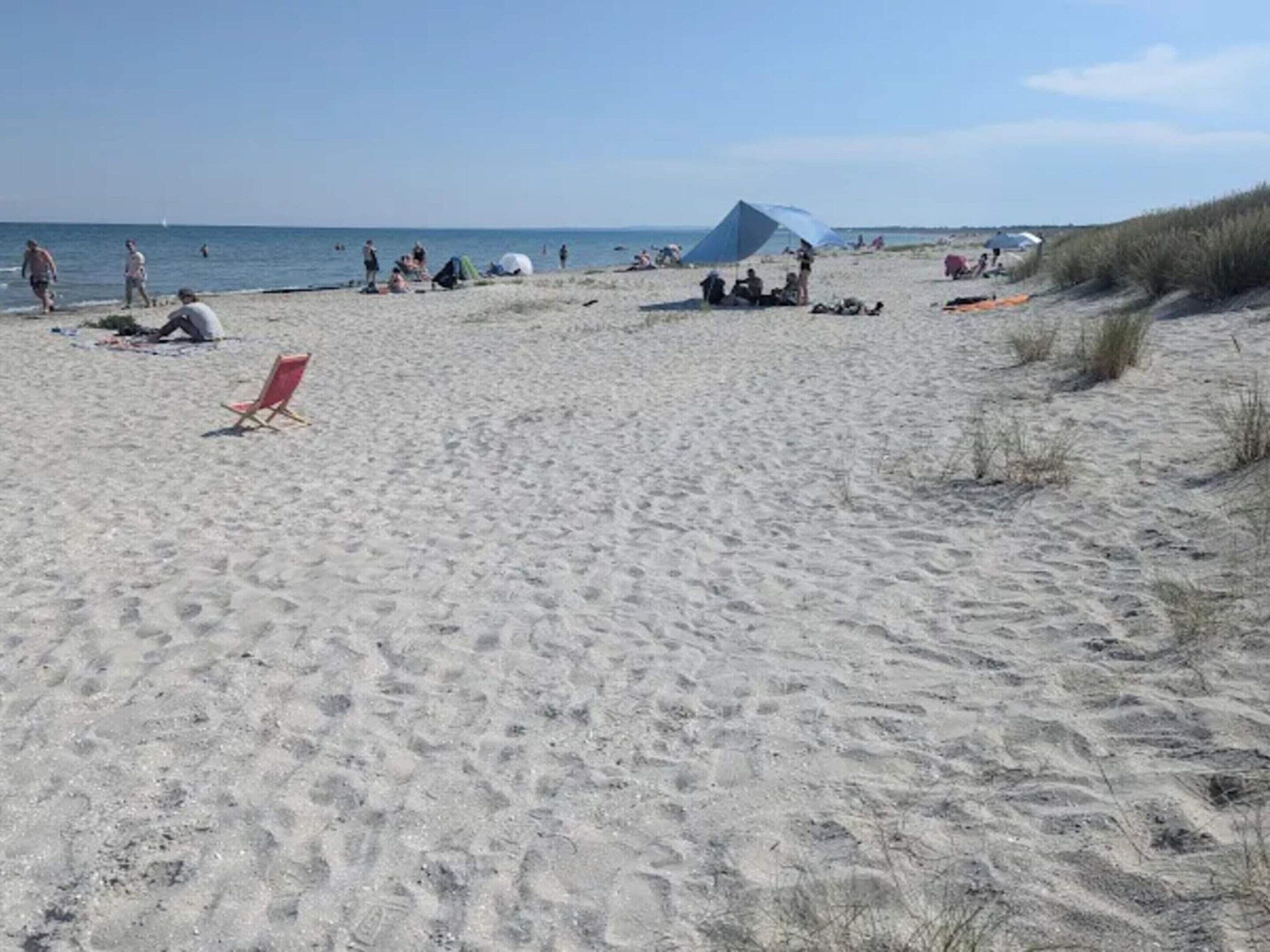 A sandy beach with a red beach chair, a blue tent, and people relaxing.