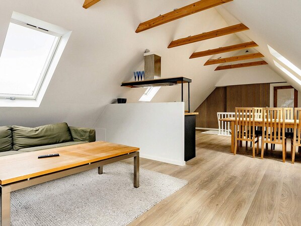 An attic room with a sloped ceiling, a dining table with chairs, a sofa, and a window.