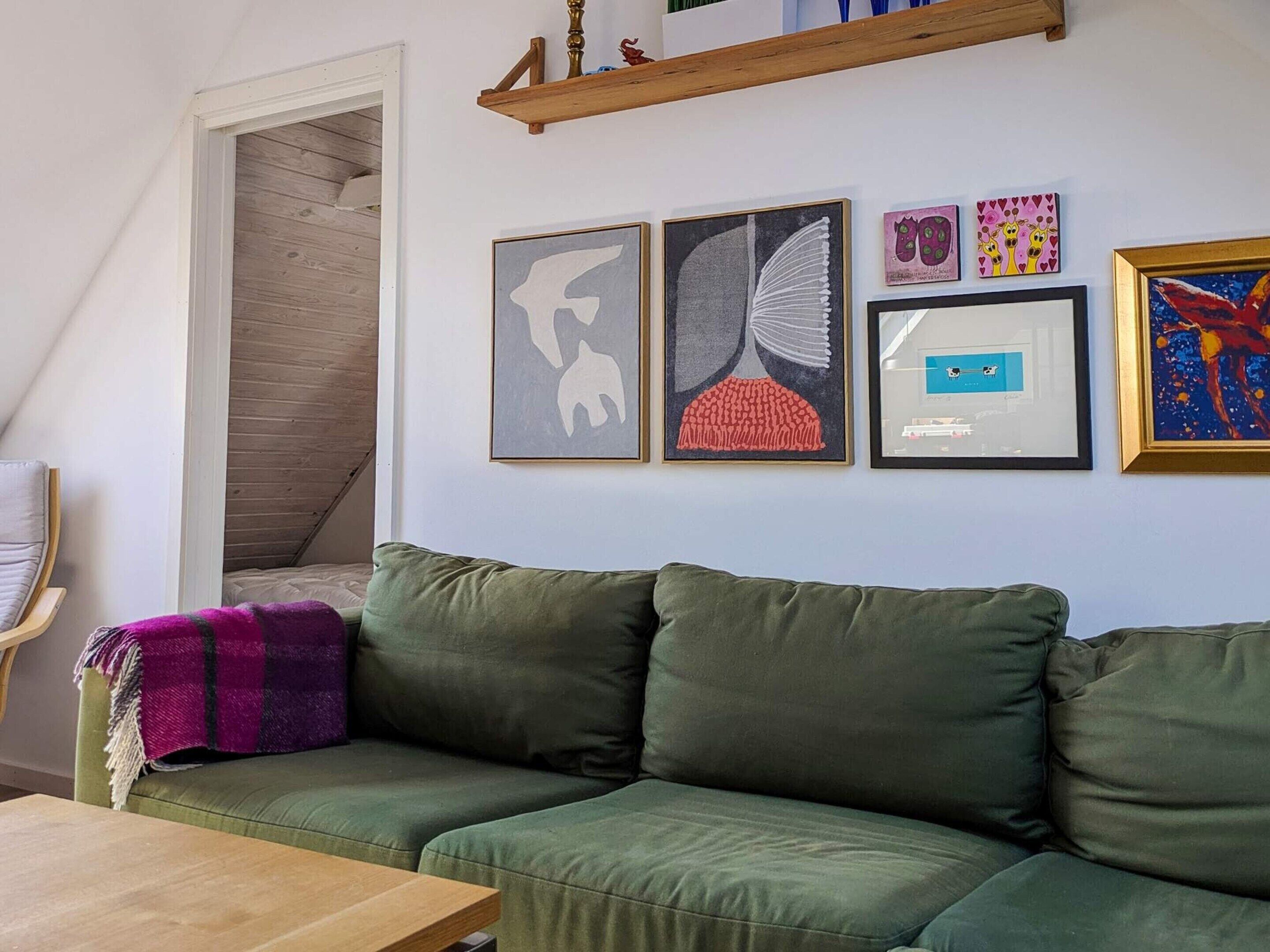 A room with a green sofa, a wooden table, and a wall with various framed artworks.