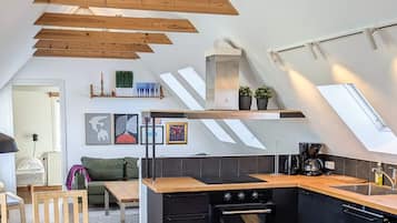 Eine moderne Küche mit schrägverdeckelter Decke, Holzbalken und einem schwarzen Herd.