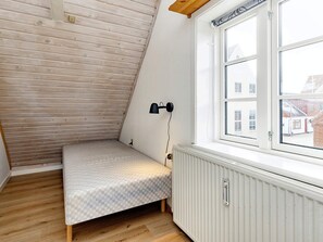 Et lille, skråt værelse med en enkelt seng, en radiator og et vindue med udsigt til bygninger.