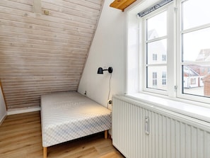 A small, sloped room with a single bed, a radiator, and a window with a view of buildings outside. - 5 Person Holiday Home in Albaek (Aalbaek)