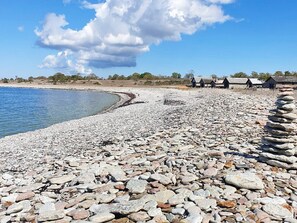 Una playa rocosa con cielo despejado y algunos edificios al fondo.