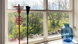 A window with a view of a natural landscape, a red and black sculpture, and a blue vase on the windowsill. - 3 Person Holiday Home in Lottorp (Löttorp)