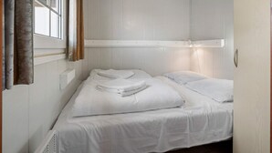 A small, single-bed room with white walls and a window with curtains.