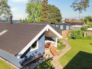 A small, single-story house with a sloped roof, a patio with a table and chairs, and a garden area. - 7 Person Holiday Home in Stroby (Strøby)