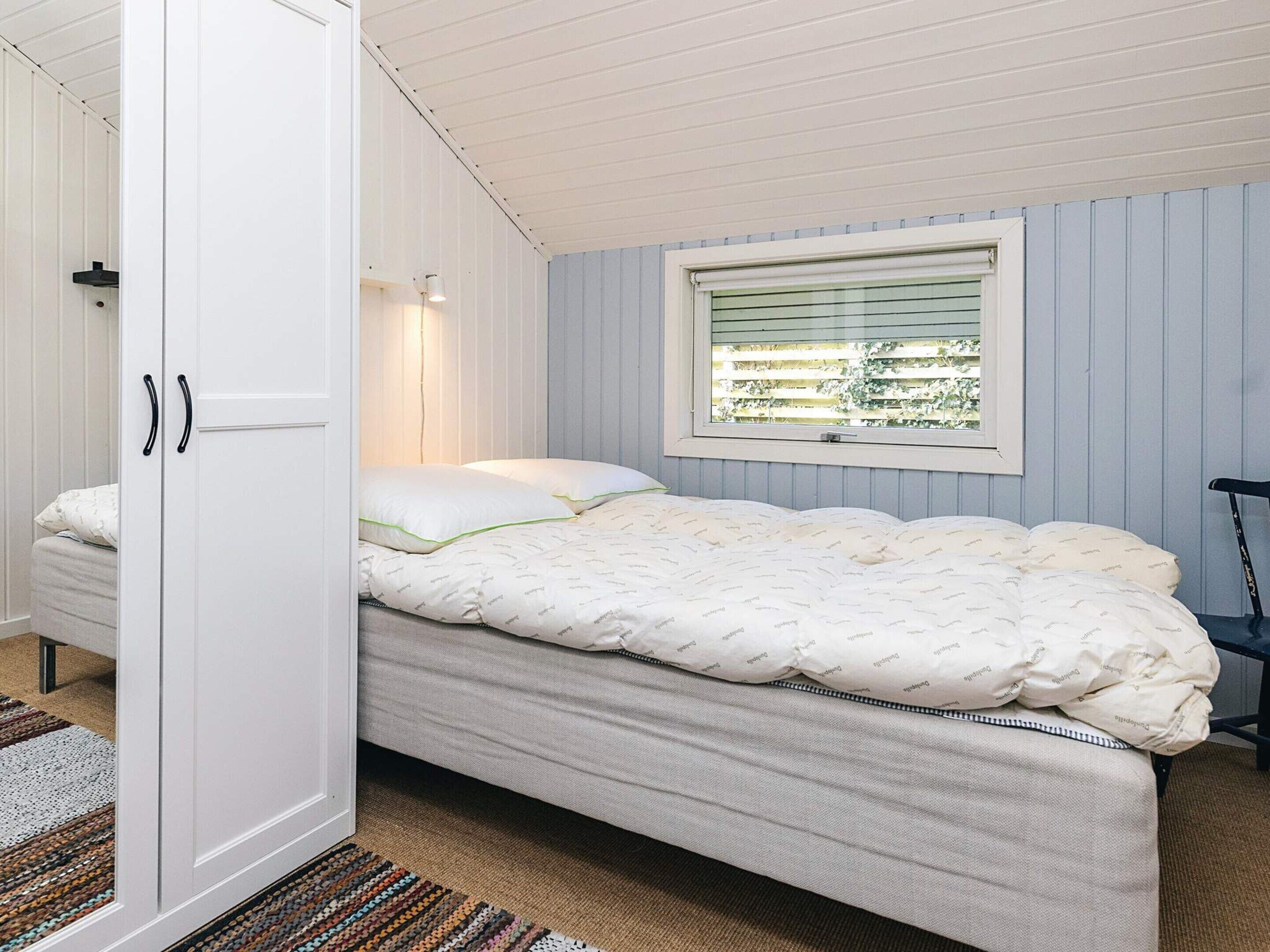 Un dormitorio con cama, ventana con persianas, una silla y un armario.