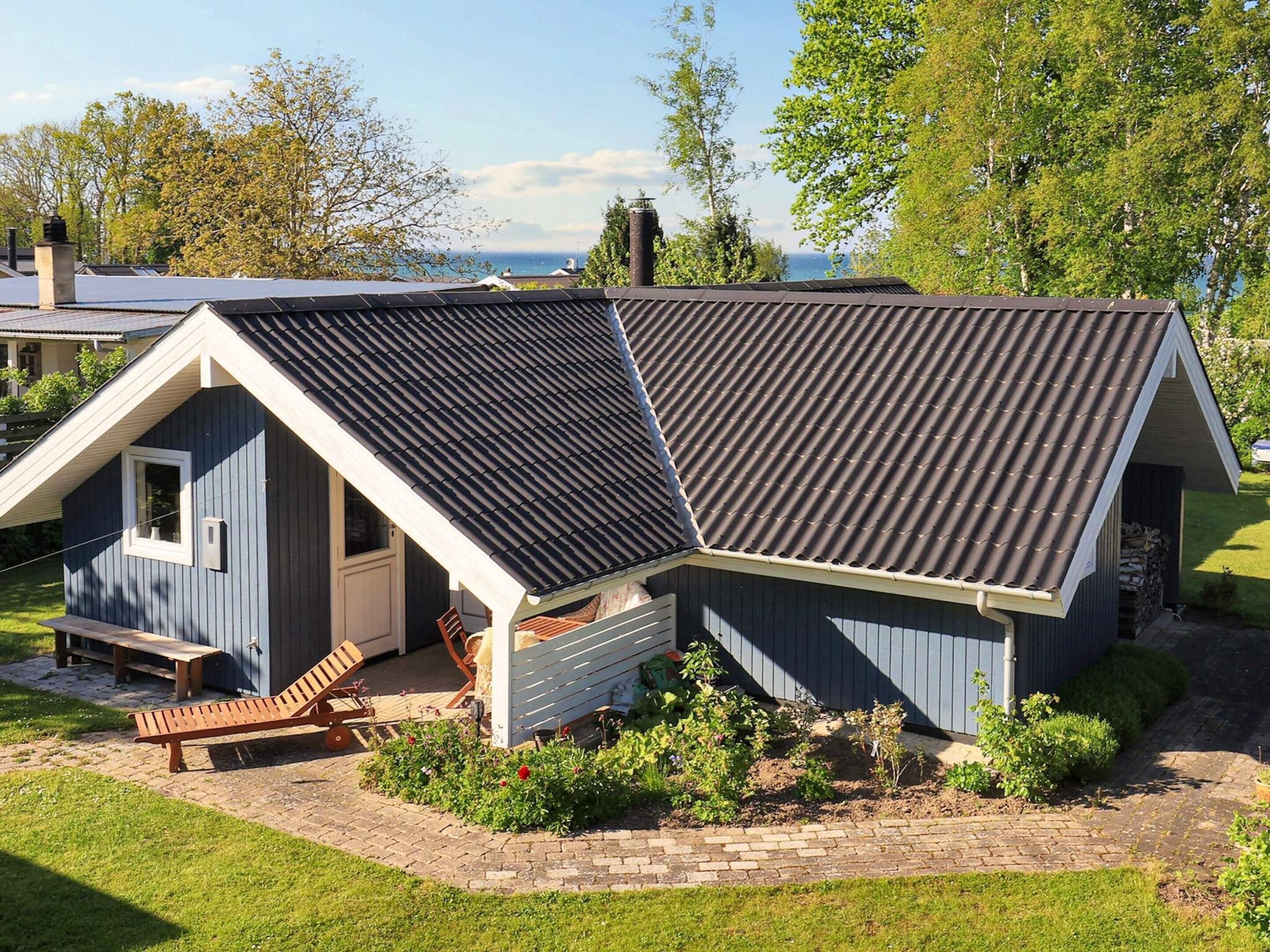 A small, single-story building with a sloped roof, a front porch with a bench, and a garden area.