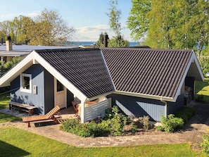 A small, single-story building with a sloped roof, a front porch with a bench, and a garden area.